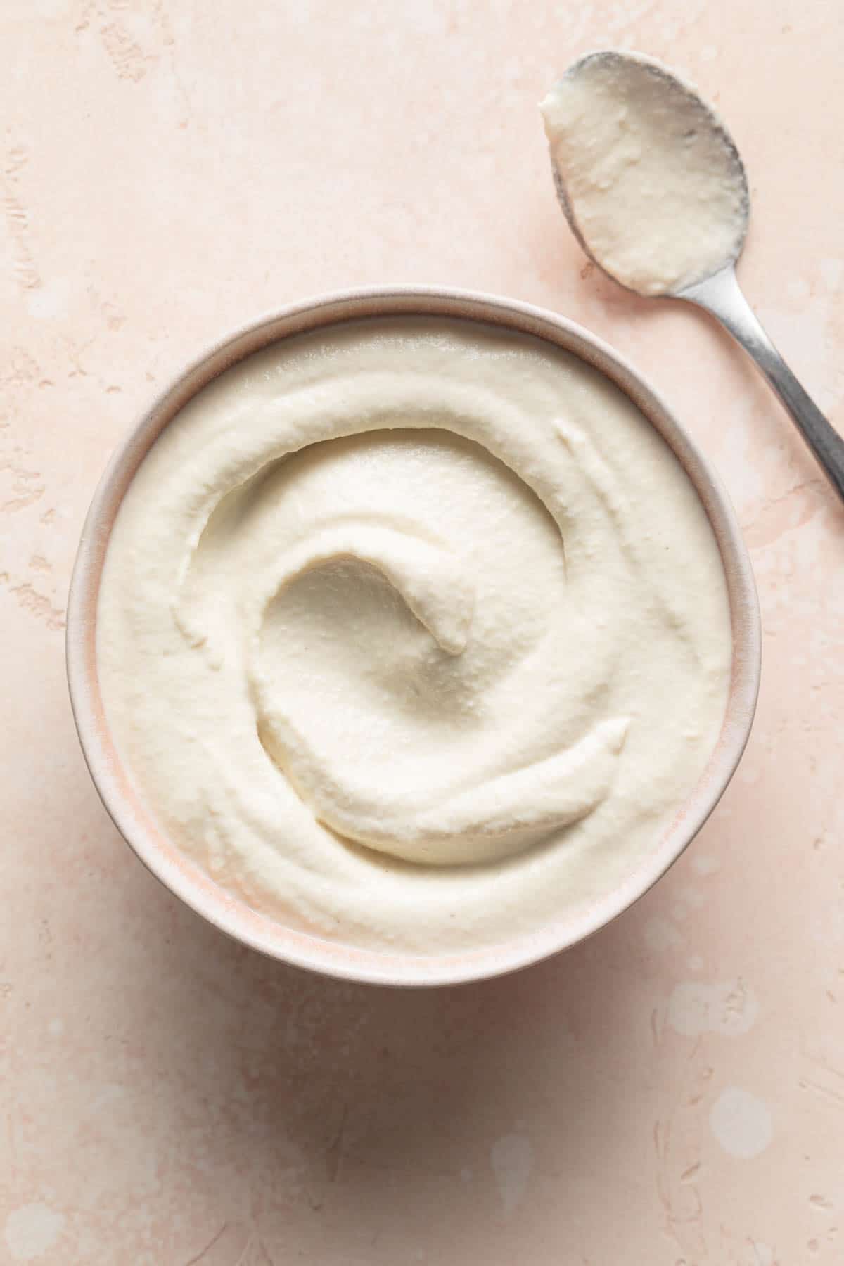 Overhead view of cashew mayo in a pink bowl with a spoon on the side.