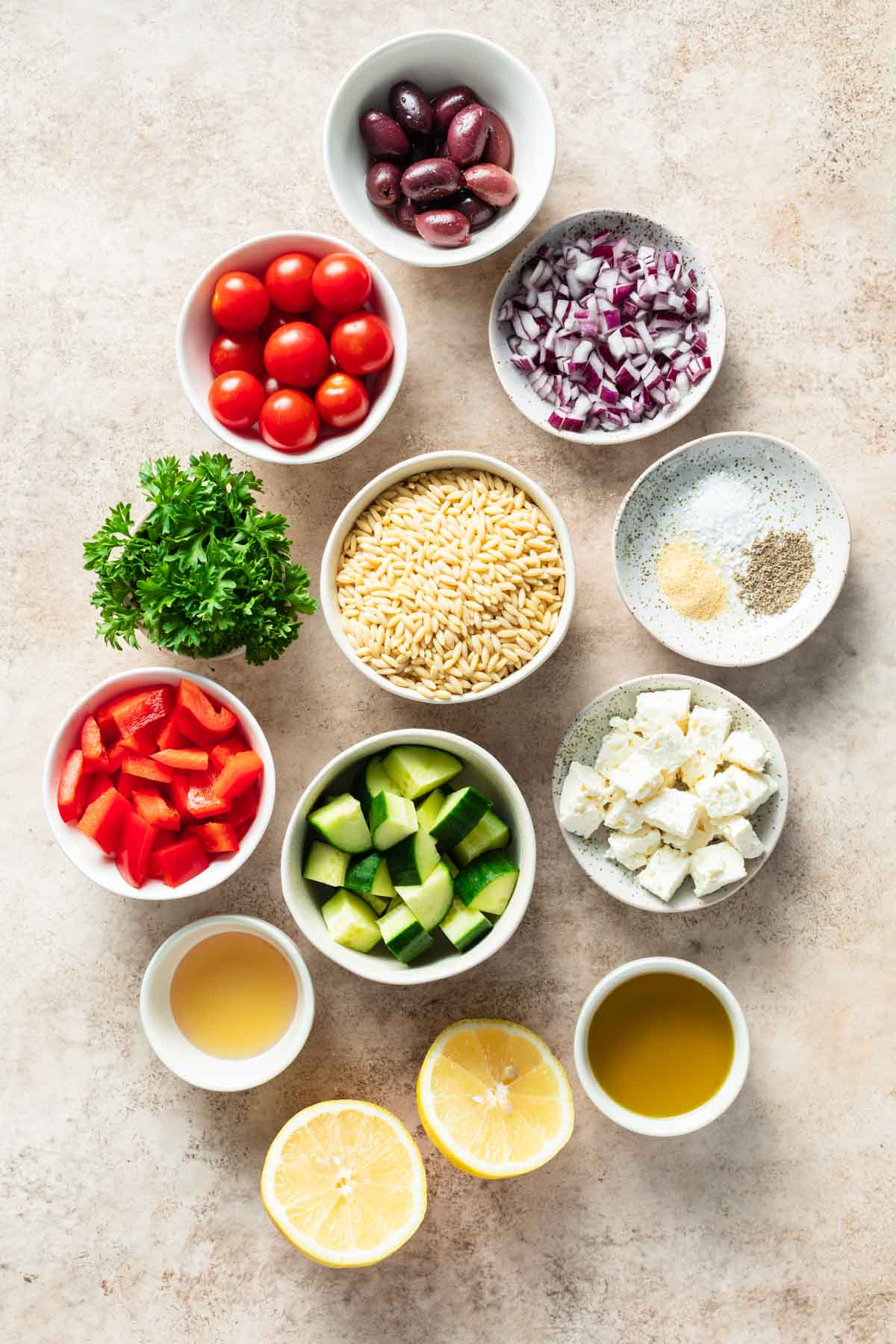 Ingredients to make Greek orzo pasta salad arranged in individual bowls.