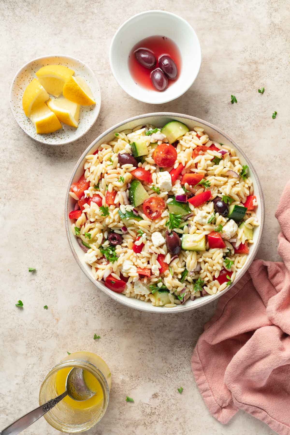 Greek orzo salad in a bowl with lemon wedges and olives on the side.