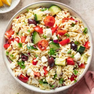 Overhead view of Greek orzo pasta salad in a white bowl with lemon vinaigrette.