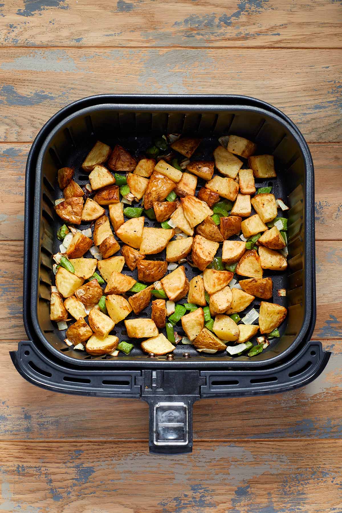 Air fried potatoes, green peppers and onions in an air fryer basket.