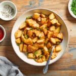 Air fryer home fries in a bowl with a spoon inserted into it.