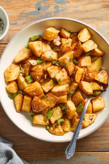 Air fryer home fries in a bowl with a spoon inserted into it.