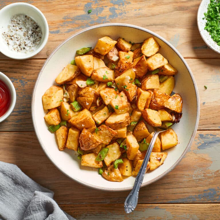 Air fryer home fries in a bowl with a spoon inserted into it.