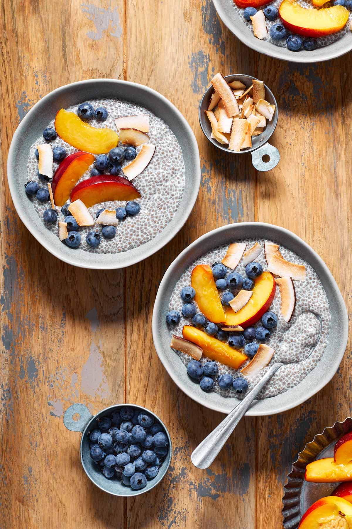 Two bowls of chia pudding topped with fruit and arranged on a wooden table.