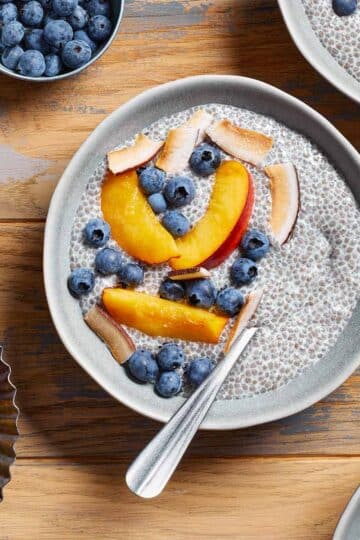 Oat milk chia pudding in a bowl with nectarine slices and blueberries on top.