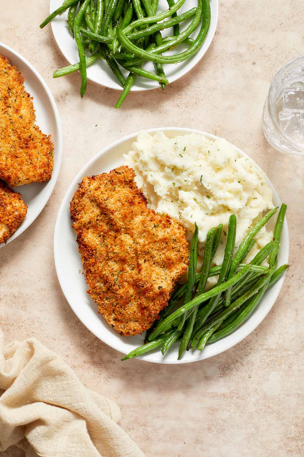 Overhead view of chicken schnitzel on a plate with green beans and mashed potatoes.