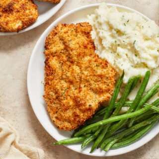 Air fryer chicken schnitzel on a white plate with mashed potatoes and green beans.