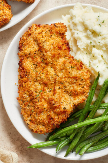 Air fryer chicken schnitzel on a white plate with mashed potatoes and green beans.