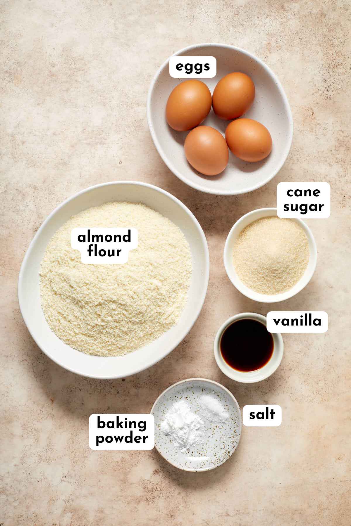 Ingredients for making vanilla almond flour cupcakes arranged individually and labeled.