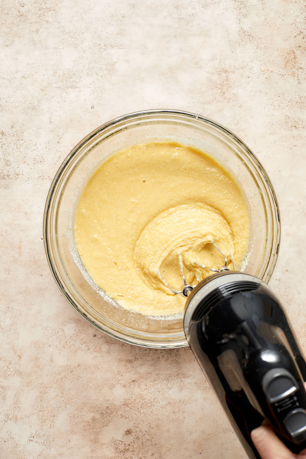 Cupcake batter mixed together in a bowl with a handheld mixer.
