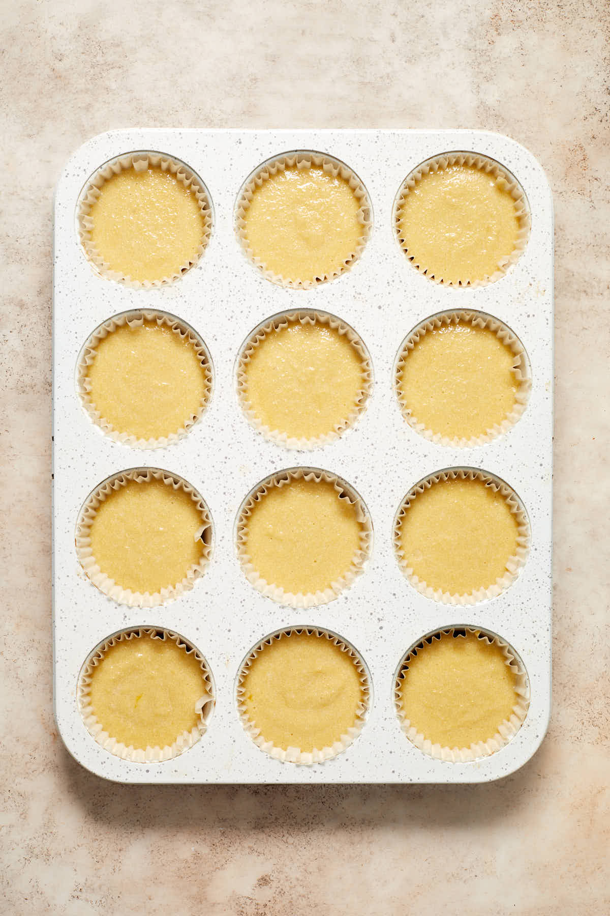 Cupcake batter divided into a 12-cavity cupcake pan with cupcake liners.