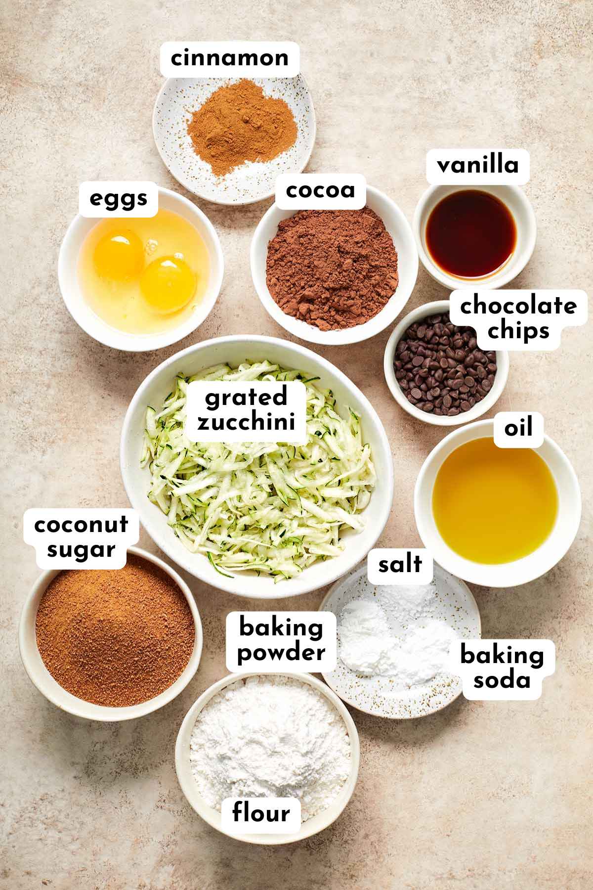 Ingredients for making chocolate zucchini cupcakes arranged in individual bowls and labeled.
