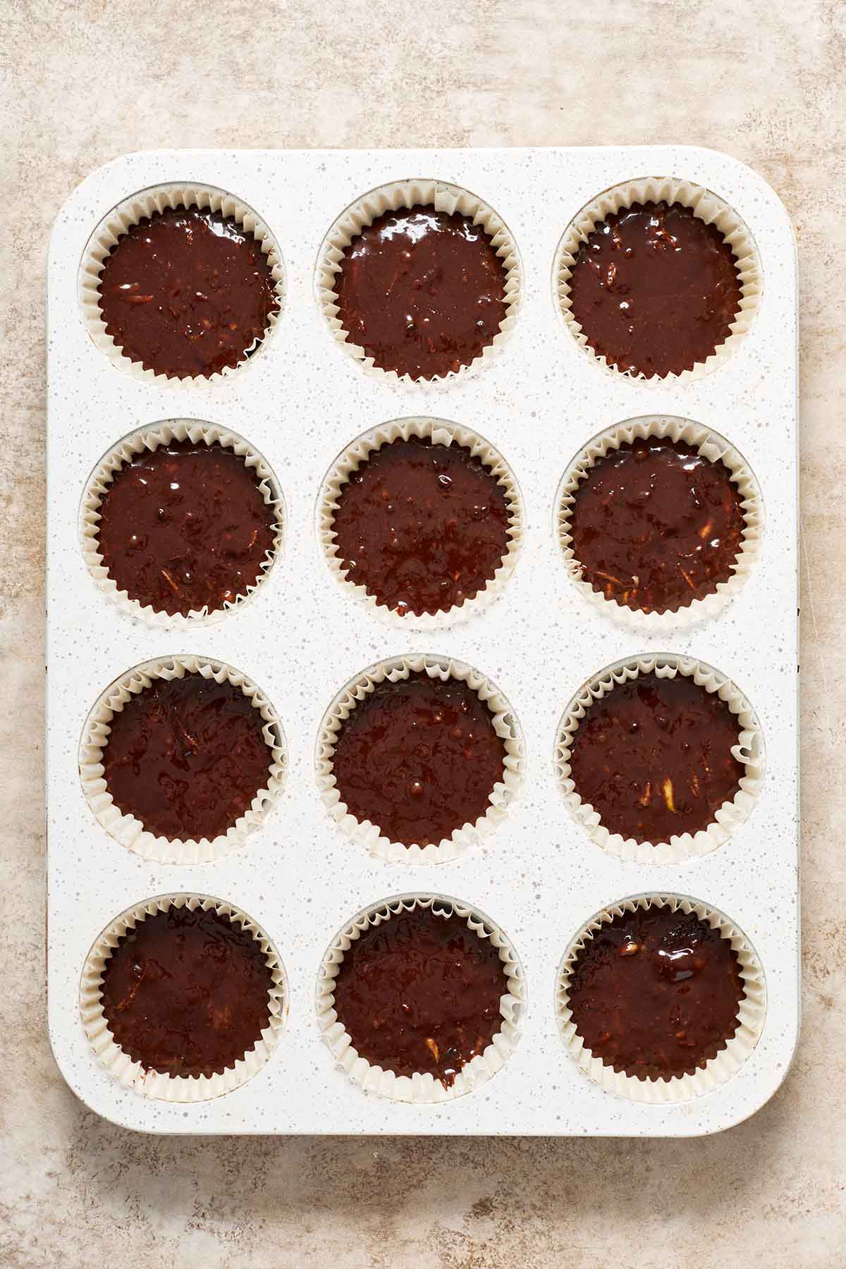 Cupcake batter added to a white 12-cavity cupcake pan lined with cupcake liners.