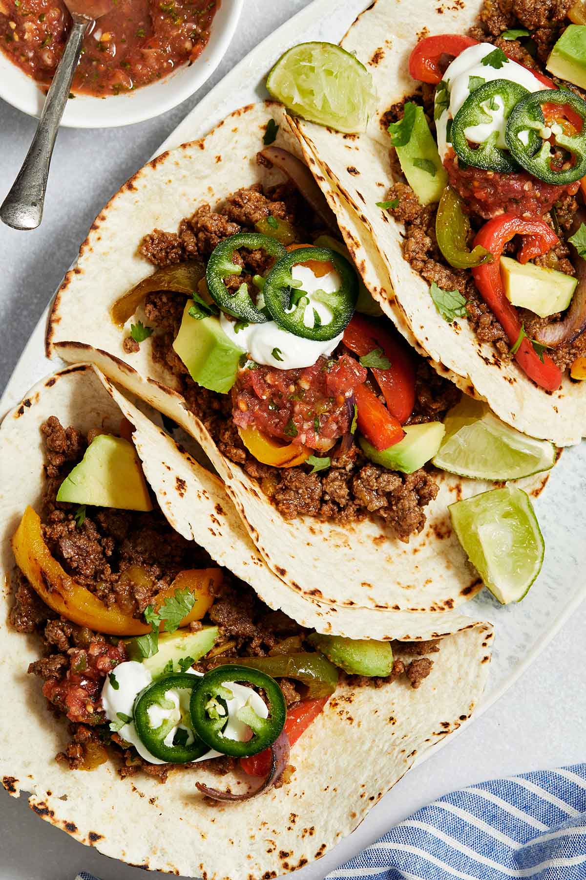 Close up view of ground beef fajitas on a platter and topped with sour cream, salsa and jalapeños.
