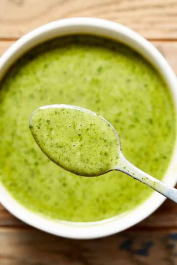 Jalapeño vinaigrette in a white bowl on a wooden table with a spoonful of vinaigrette lifted out of the bowl.