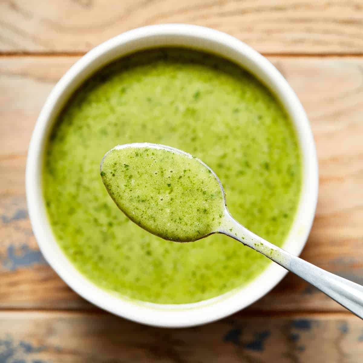 Jalapeño vinaigrette in a white bowl on a wooden table with a spoonful of vinaigrette lifted out of the bowl.