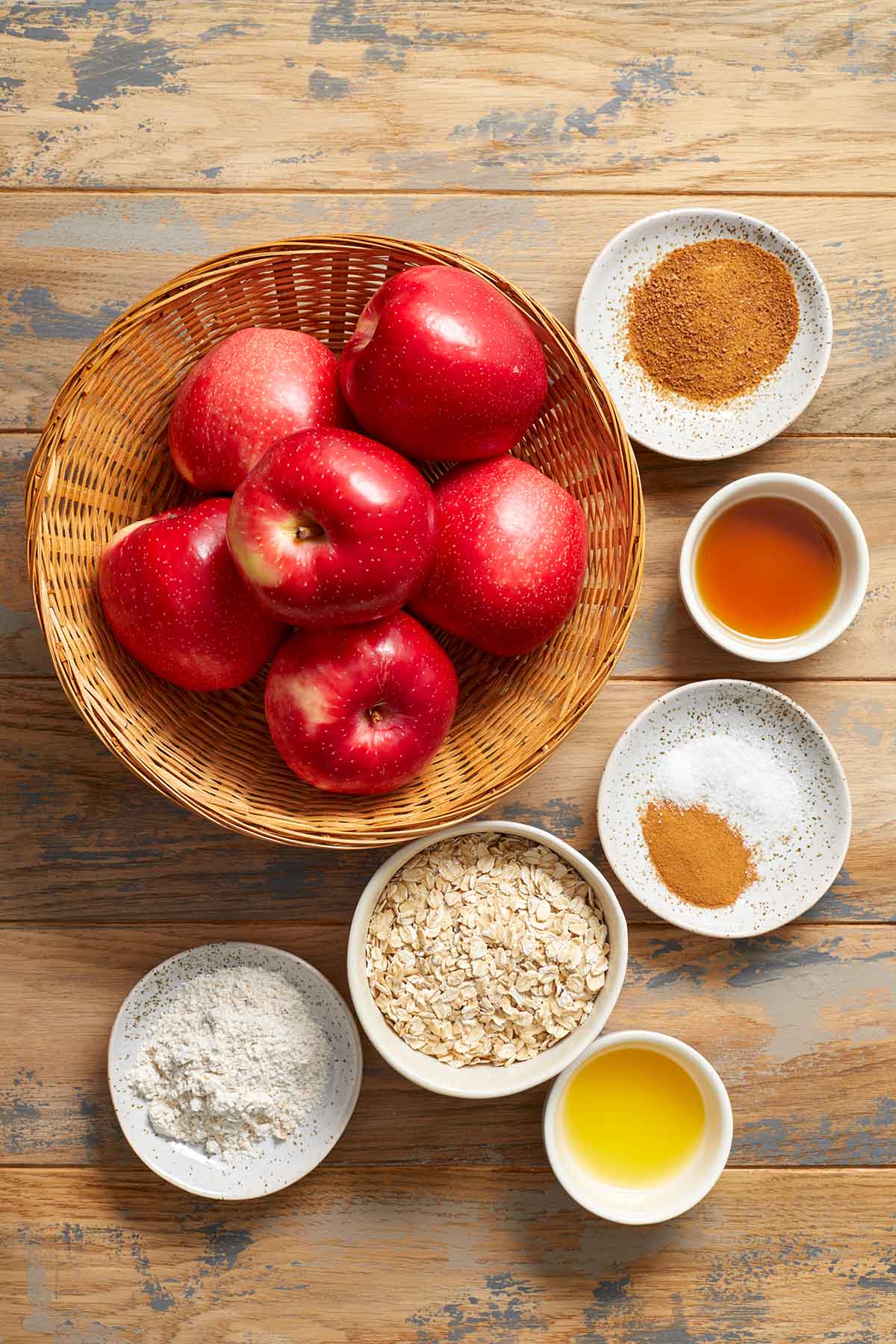 Ingredients to make air fryer apples arranged individually on a wooden surface.