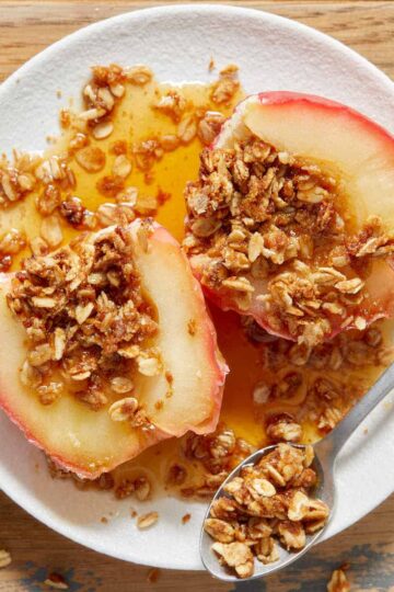 An air fryer baked apple cut in half and served on a white plate with maple syrup.