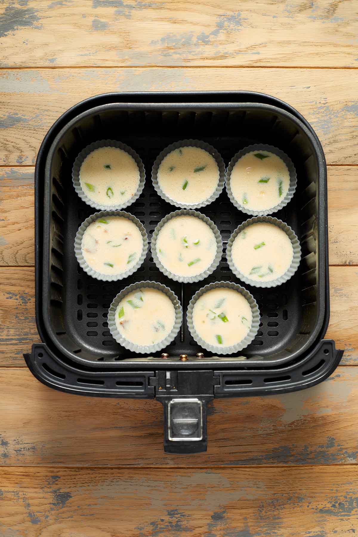 Silicone muffin cups filled with egg mixture and placed in the air fryer basket.