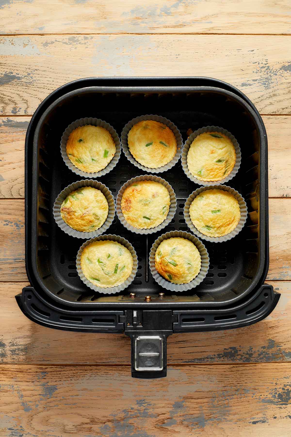 Cooked egg bites in muffin cups in the air fryer basket.