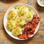 Air fryer egg bites on a white plate with slices of bacon.
