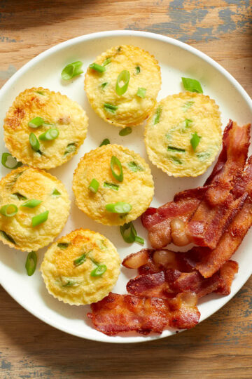 Air fryer egg bites on a white plate with slices of bacon.