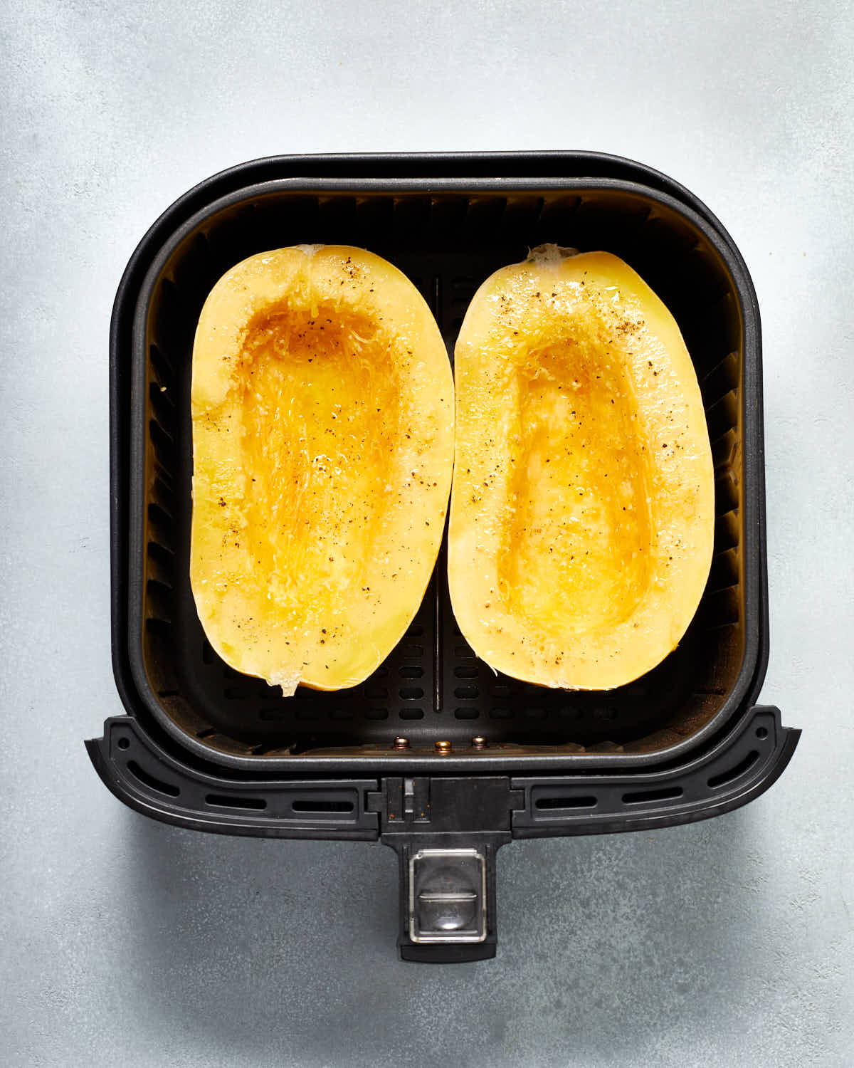 Squash halves with oil and seasonings arranged cut side up in the air fryer basket.