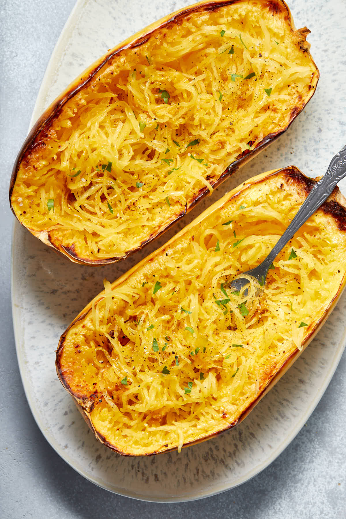 Up close view of two roasted spaghetti squash halves on a platter with some noodles twirled around a fork.