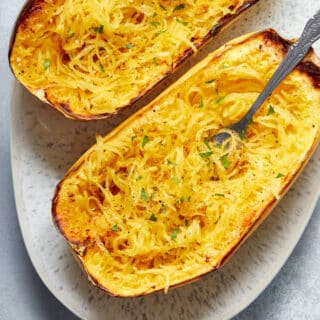Air fryer spaghetti squash halves on a platter with a fork inserted into some noodles.