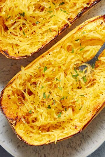 Air fryer spaghetti squash halves on a platter with a fork inserted into some noodles.
