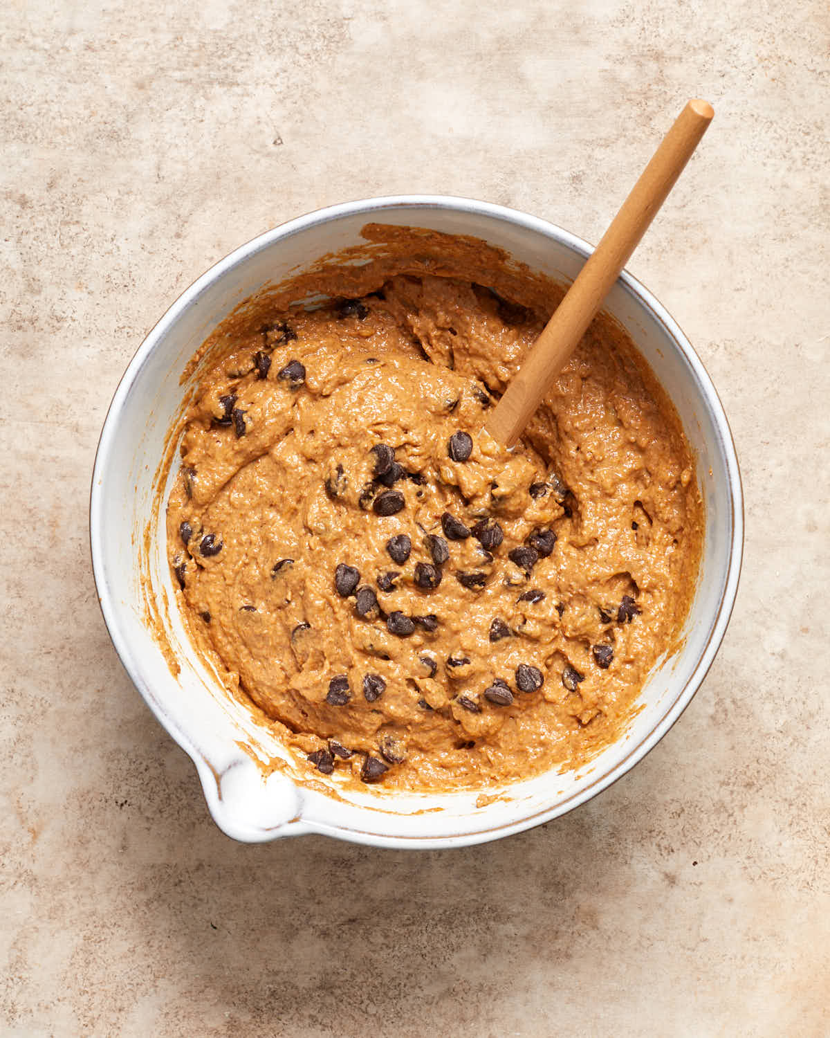 Pumpkin banana bread batter in a bowl with chocolate chips stirred into it with a spatula.