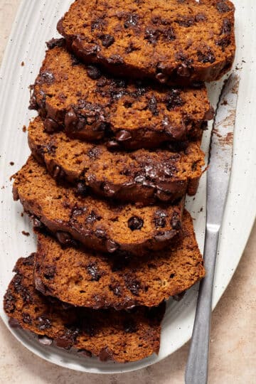 Slices of pumpkin banana bread on a white platter with a knife next to it.