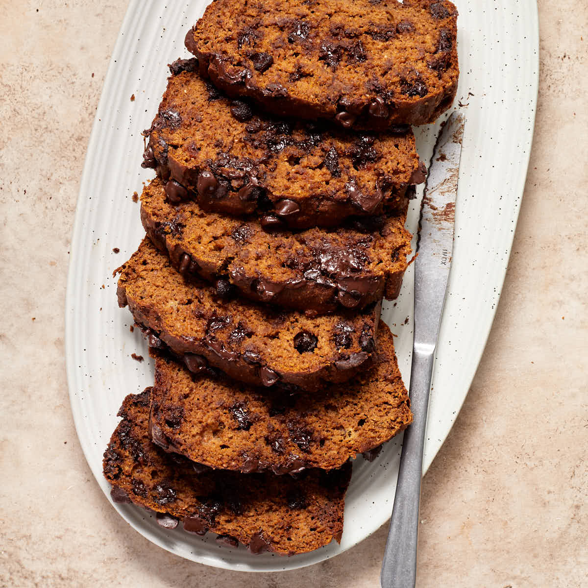 Slices of pumpkin banana bread on a white platter with a knife next to it.