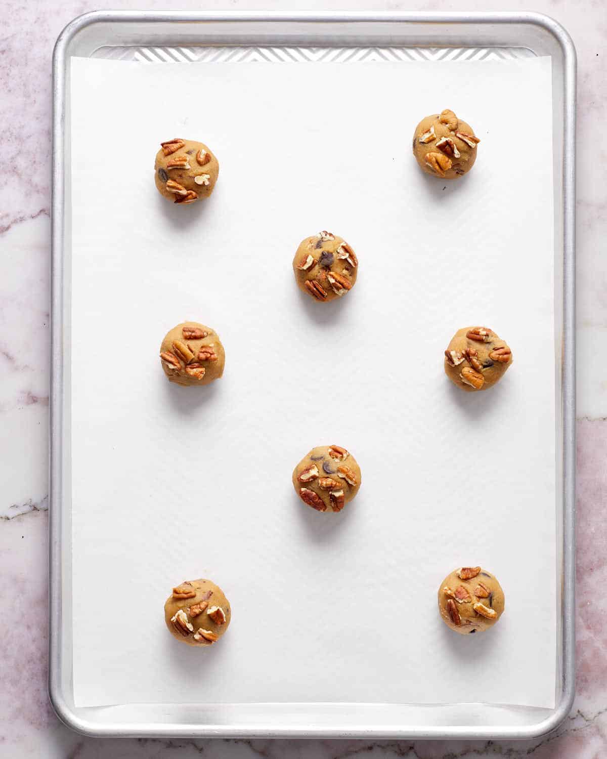 Cookie dough rolled into balls and arranged on a parchment paper lined baking sheet.