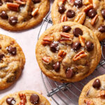 Close up view of a chocolate chip pecan cookie on a wire cooling rack.