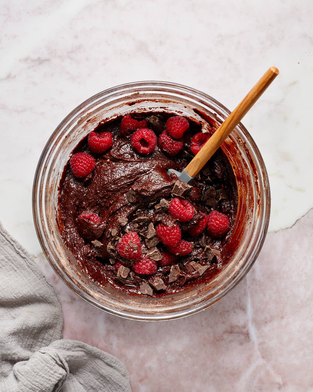 Brownie batter in a glass bowl with raspberries and chopped chocolate stirred in.