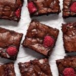Raspberry brownies cut into squares and arranged on white parchment paper.