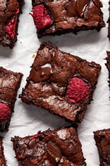 Raspberry brownies cut into squares and arranged on white parchment paper.