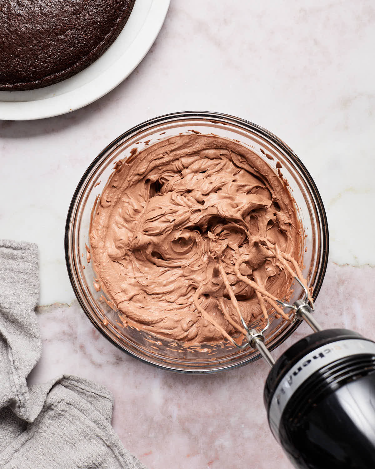 Chocolate whipped cream frosting being whipped together with an electric mixer in a glass bowl.