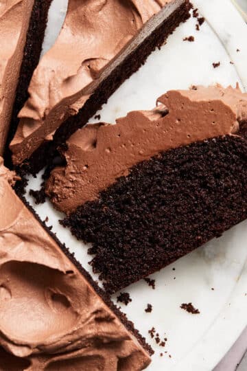 Close up view of a slice of almond flour chocolate cake on a white marble cake plate.