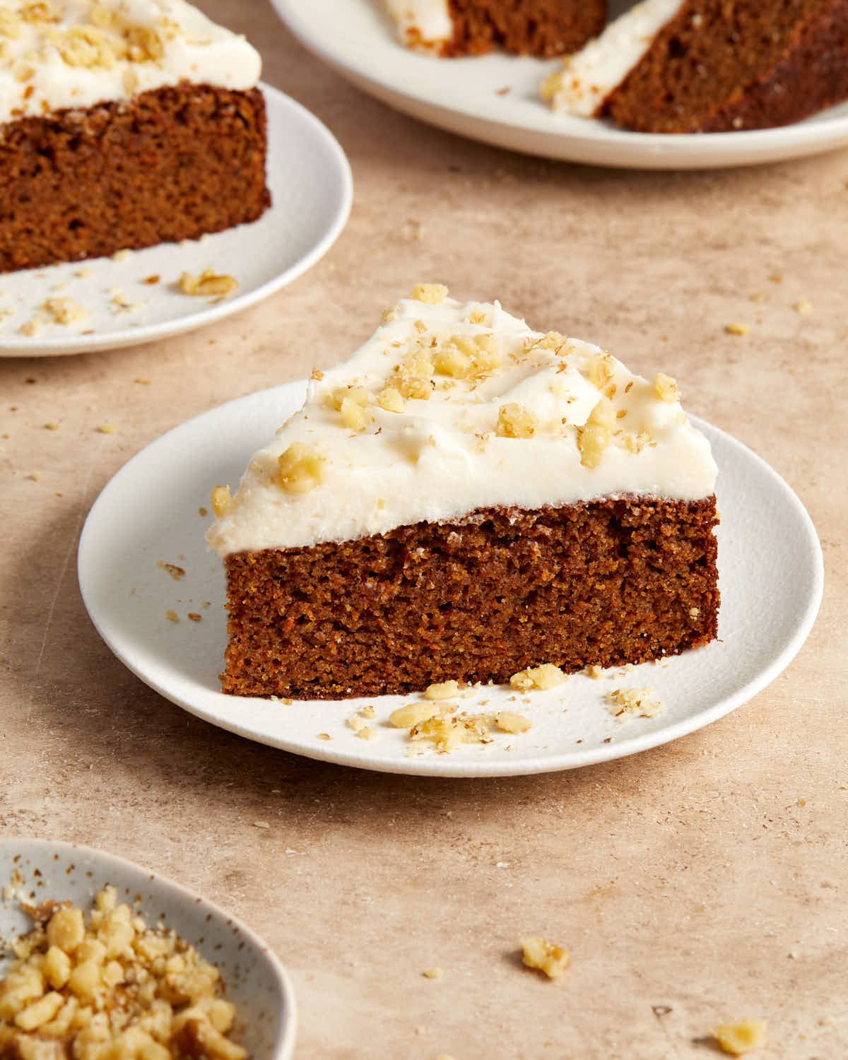 Side view of a slice of carrot cake on a white plate with more slices in the background.