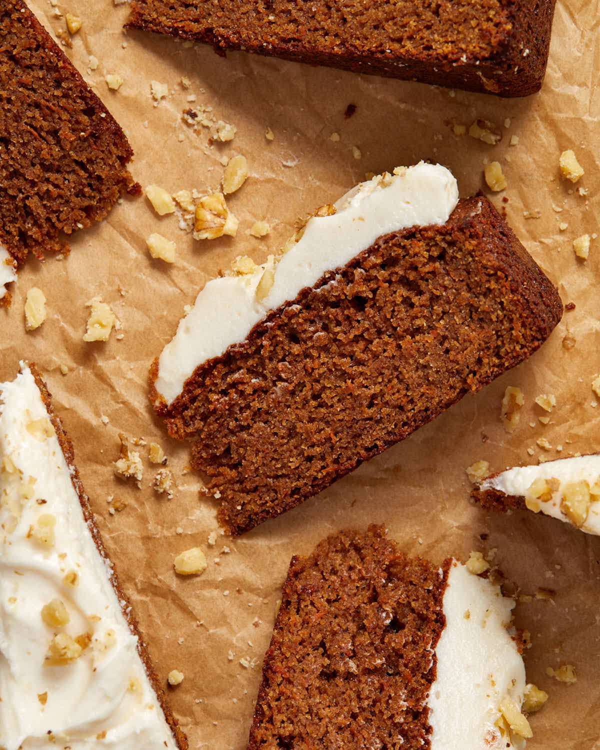 Overhead close up view of a slice of carrot cake on brown parchment paper.