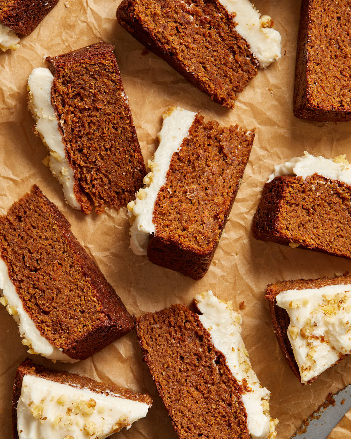 Overhead view of multiple slices of carrot cake arranged on crumpled brown parchment paper.