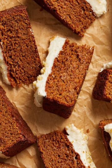 Slices of almond flour carrot cake with dairy free cream cheese frosting arranged on crumpled brown parchment paper.
