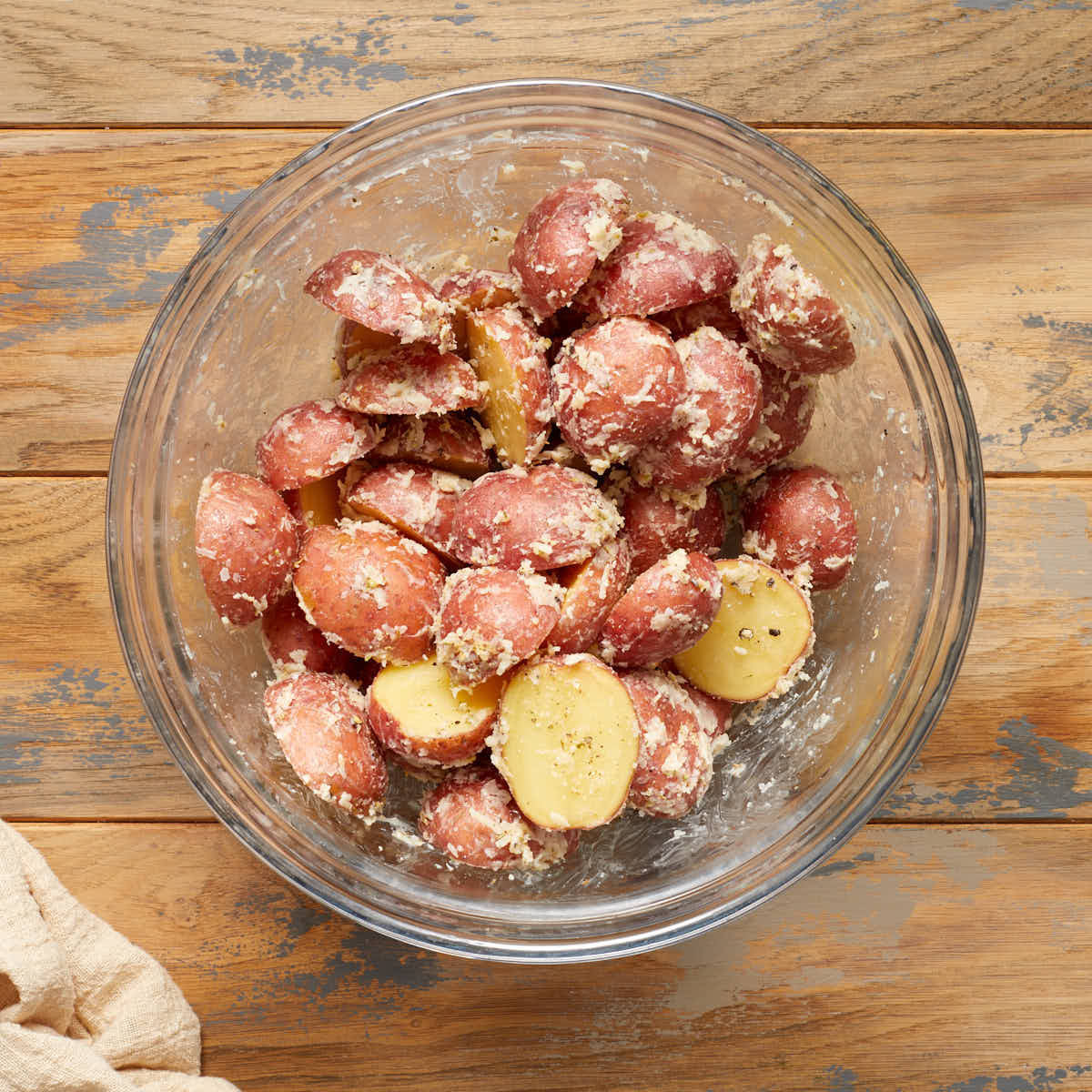 Baby potatoes cut in half in a glass bowl and coated in parmesan mixture.