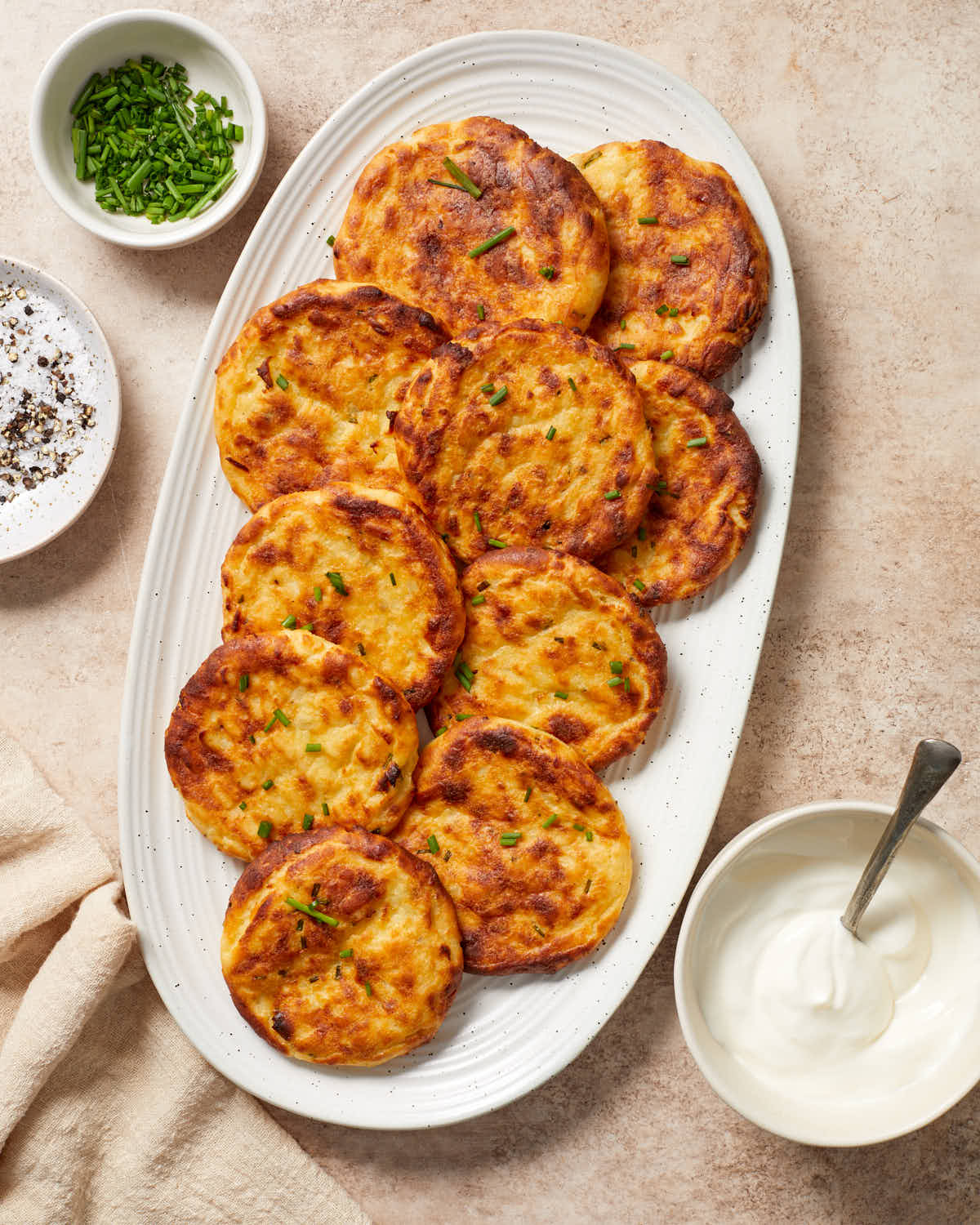 Golden brown and crispy potato cakes arranged on a white oval platter.