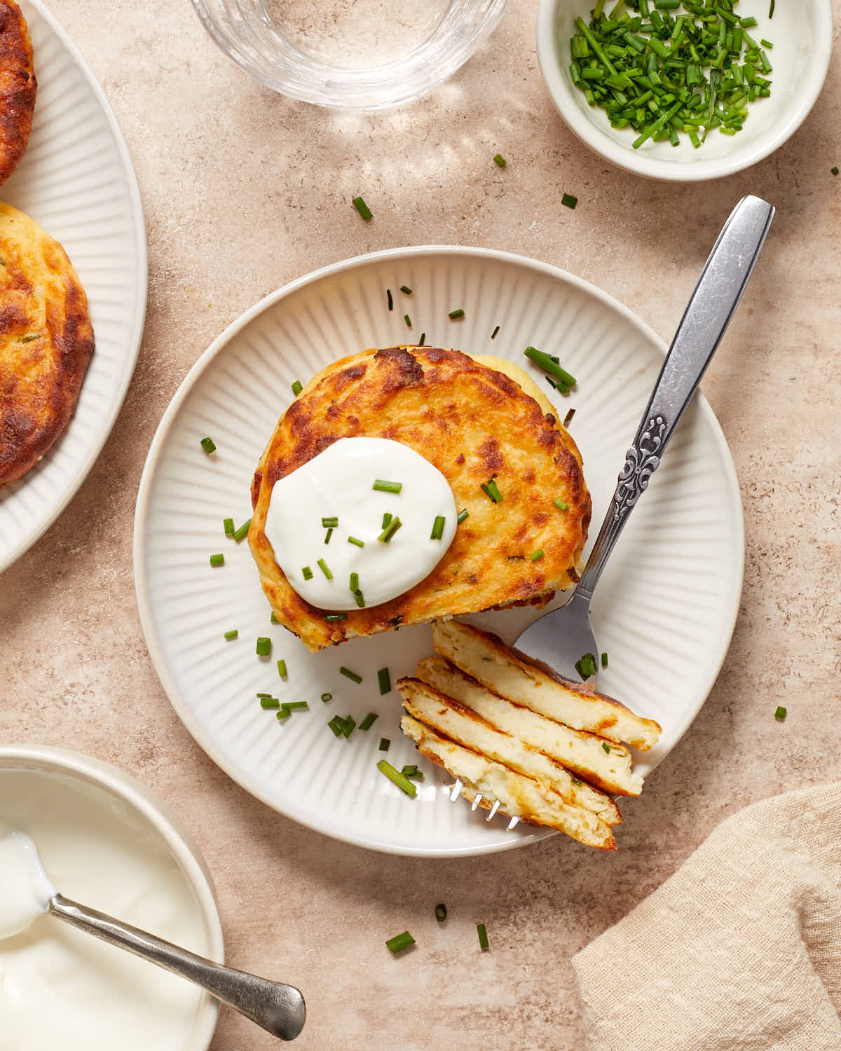Overhead view of a stack of potato cakes on a white plate with a dollop of sour cream on top and chopped chives.