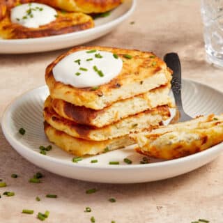 Stack of air fryer potato cakes on a plate with a dollop of sour cream and chopped chives on top.