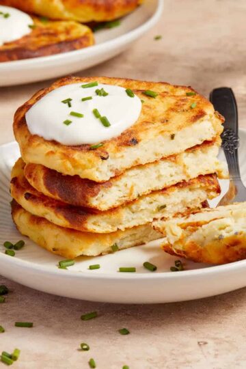 Stack of air fryer potato cakes on a plate with a dollop of sour cream and chopped chives on top.